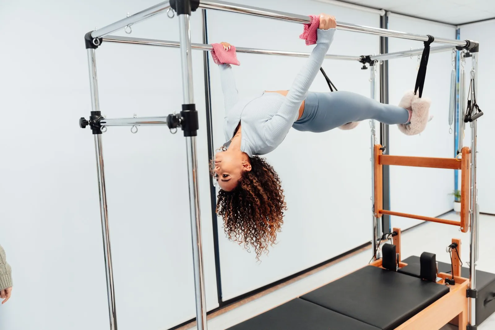 A woman exercising on a Pilates tower while wearing pink grip socks